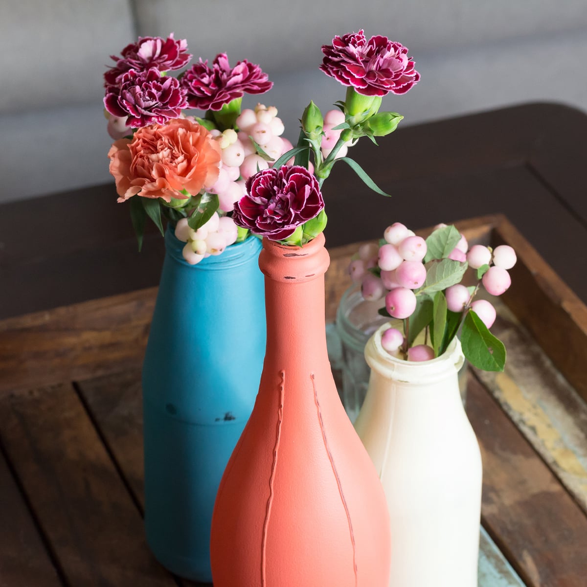 Mit Kreidefarbe bemalte Vasen aus alten Glasflaschen im Landhaus-Stil auf Holztisch